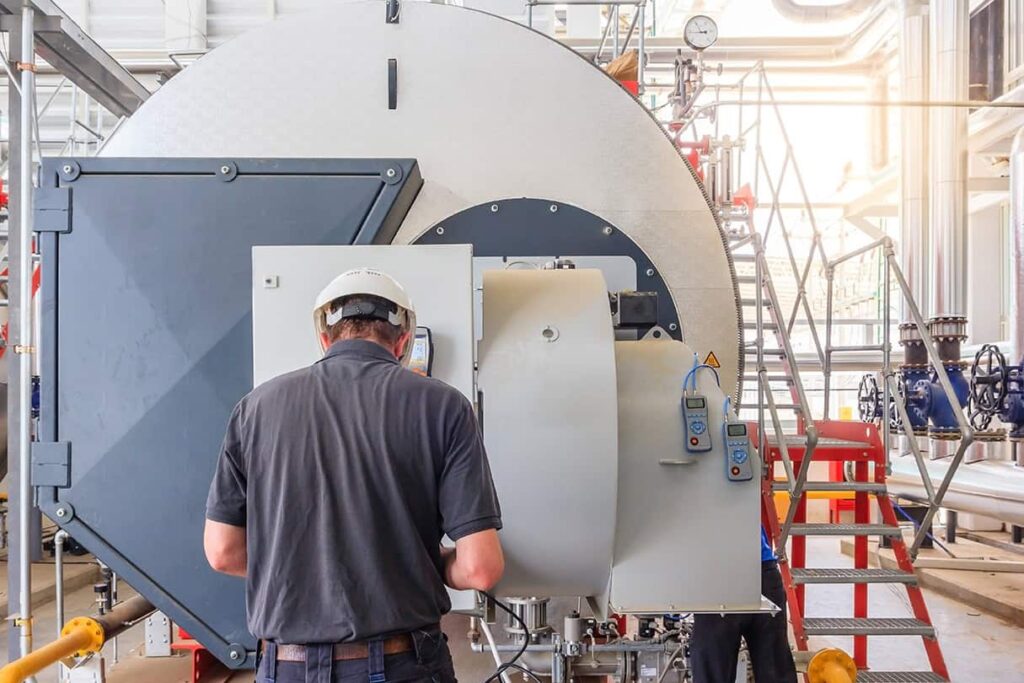 An industrial technician inspects a large commercial boiler with monitoring devices attached.