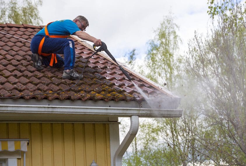 Man pressure-washing moss off a tiled roof.