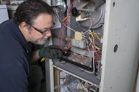 An HVAC technician inspects wiring inside an open furnace unit.